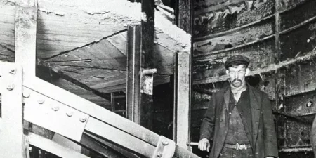 Two workmen stand with the spiral escalator at Holloway Road station; image courtesy of London Transport Museum.