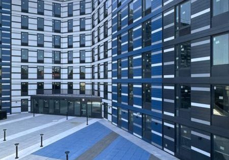 The building's exterior is composed of white, gray and blue paneling surrounding a grid of rectangular floor-to-ceiling windows; photo by Michael Young for New York YIMBY.