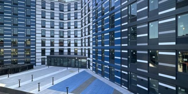 The building's exterior is composed of white, gray and blue paneling surrounding a grid of rectangular floor-to-ceiling windows; photo by Michael Young for New York YIMBY.